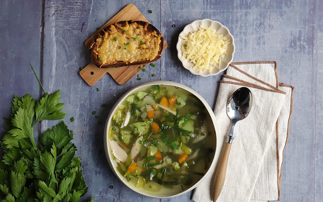 Bol de soupe microbiote friendly aux légumes verts avec une tartine gratinée et fromage râpé, un plat sain pour renforcer la santé intestinale.