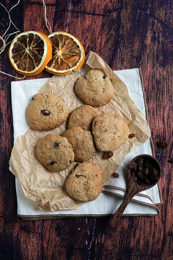 recette de Cookies d’automne aux raisins secs sur un papier parchemin avec des tranches d’orange séchée.