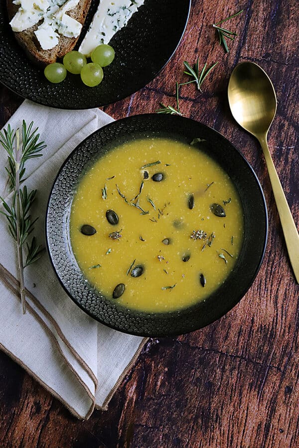 Soupe crémeuse à la courge servie dans un bol noir avec des graines et des herbes.