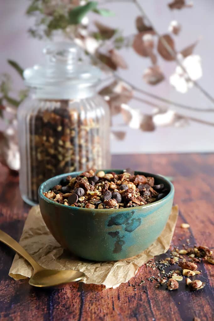 Bol de granola microbiote friendly sans farine et sans sucre raffiné, présenté dans un bol vert sur une table en bois, avec un pot de granola en arrière-plan.